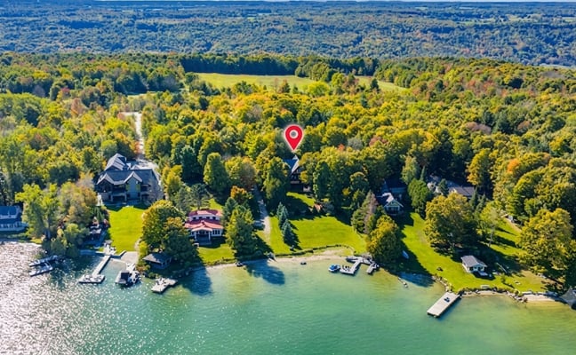 Aerial view of lakefront homes surrounded by dense forest with a red location pin marking a property